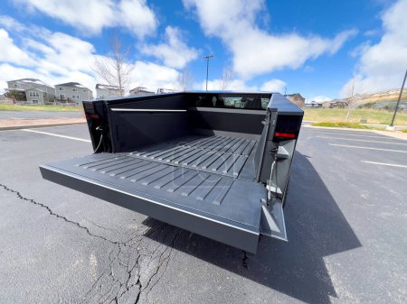 Photo for Denver, Colorado, USA-March 28, 2024-The distinctive rear end of a Tesla Cybertruck, captured in an empty parking lot, stands out against a backdrop of suburban homes under a blue sky with fluffy - Royalty Free Image