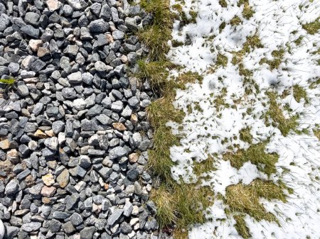 Une image montrant les vestiges d'une tempête de neige printanière sur un paysage suburbain, où la neige fondante rencontre les textures contrastées du gravier et de l'herbe verte.