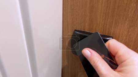 Nahaufnahme der Hand eines Gastes, der eine schwarze Schlüsselkarte benutzt, um eine Hotelzimmertür zu entriegeln, was die Sicherheit und den Komfort moderner Hotelzugangssysteme demonstriert.