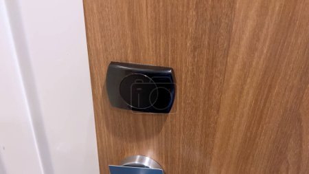 Vista de cerca de una mano de huésped usando una tarjeta de llave negra para abrir la puerta de una habitación de hotel, lo que demuestra la seguridad y conveniencia de los modernos sistemas de acceso al hotel.