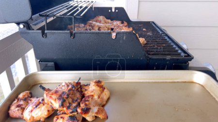 Téléchargez les photos : Une image en gros plan capturant le processus de grillage des morceaux de poulet marinés, avec une personne les retournant habilement pour assurer une cuisson uniforme sur un barbecue extérieur classique. - en image libre de droit