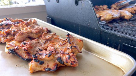 Une image en gros plan capturant le processus de grillage des morceaux de poulet marinés, avec une personne les retournant habilement pour assurer une cuisson uniforme sur un barbecue extérieur classique.