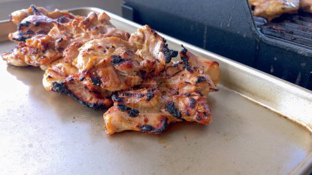 A close-up image capturing the process of grilling marinated chicken pieces, with a person expertly flipping them to ensure even cooking on a classic outdoor barbecue grill.