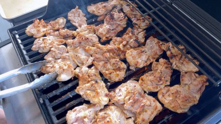 Una imagen de primer plano que captura el proceso de asar piezas de pollo marinado, con una persona expertamente voltearlas para asegurar incluso cocinar en una parrilla de barbacoa al aire libre clásica.