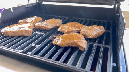 Photo for Several thick steaks with grill marks cooking to perfection on an outdoor grill, capturing the essence of a sunny barbecue day. - Royalty Free Image