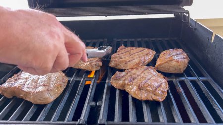 Mehrere dicke Steaks mit Grill markieren das Kochen in Perfektion auf einem Outdoor-Grill und fangen die Essenz eines sonnigen Grilltages ein.