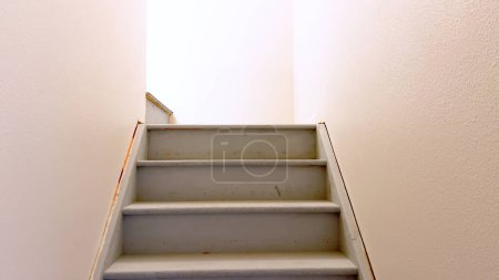Photo for View of a plain white painted staircase descending into the basement of a house, characterized by its clean lines and minimalistic design. - Royalty Free Image
