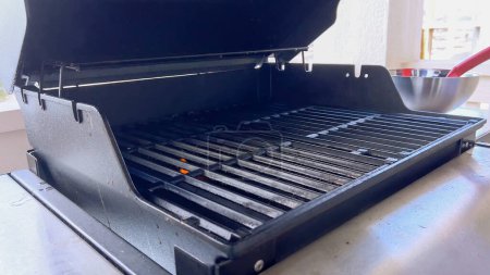 Photo for A hand uses a red grill brush to clean the black grates of a barbecue grill, ensuring it remains in perfect condition for the next grilling session. - Royalty Free Image