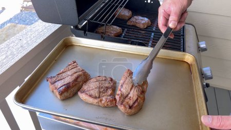 Varios filetes gruesos con marcas de parrilla cocinando a la perfección en una parrilla al aire libre, capturando la esencia de un día de barbacoa soleado.