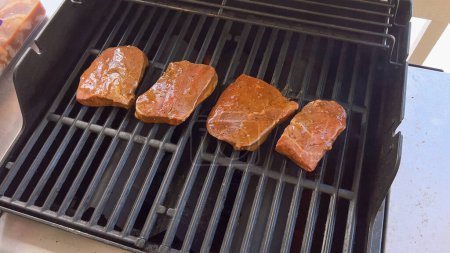 Several thick steaks with grill marks cooking to perfection on an outdoor grill, capturing the essence of a sunny barbecue day.