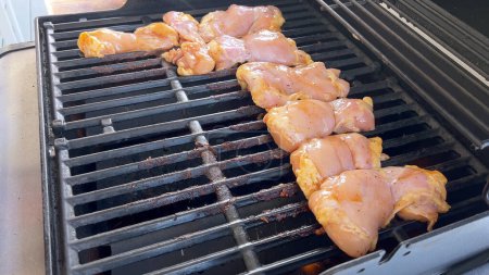 Téléchargez les photos : Une image en gros plan capturant le processus de grillage des morceaux de poulet marinés, avec une personne les retournant habilement pour assurer une cuisson uniforme sur un barbecue extérieur classique. - en image libre de droit