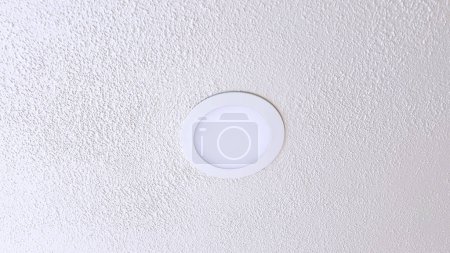 Foto de Un accesorio de luz de techo simple y moderno se coloca centralmente contra un techo blanco texturizado, proporcionando una iluminación limpia y eficiente dentro de una habitación. - Imagen libre de derechos