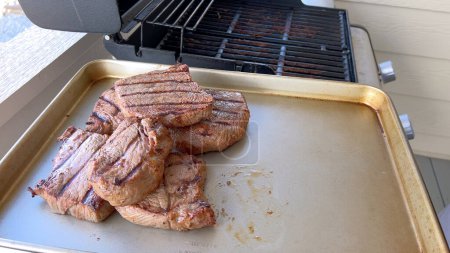 Téléchargez les photos : Several thick steaks with grill marks cooking to perfection on an outdoor grill, capturing the essence of a sunny barbecue day. - en image libre de droit