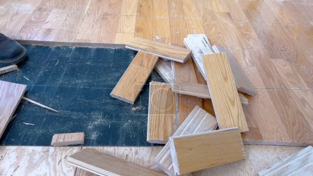 Eine verstreute Reihe von Laubholzdielen liegt auf einem teilweise abgeschlossenen Fußboden und unterstreicht die laufenden Arbeiten eines Renovierungsprojekts, das sich auf die Verlegung neuer Holzböden konzentriert..