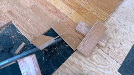 Eine verstreute Reihe von Laubholzdielen liegt auf einem teilweise abgeschlossenen Fußboden und unterstreicht die laufenden Arbeiten eines Renovierungsprojekts, das sich auf die Verlegung neuer Holzböden konzentriert..