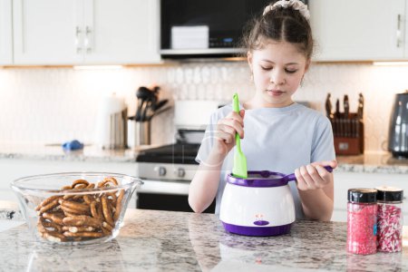 Photo for With focused attention, this budding culinary artist dips pretzels into a pot of melted chocolate, creating sweet delights in the warmth of a well-lit home kitchen. - Royalty Free Image