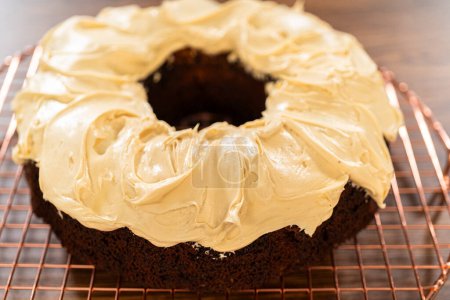 A gingerbread bundt cake being generously frosted with salted caramel frosting and topped with delightful gingerbread sprinkles.