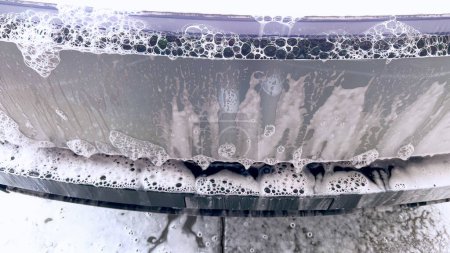 Foto de Un Cybertruck Tesla se somete a un lavado a fondo, su exterior único y angular cubierto de jabón suds, destacando el diseño elegante del vehículo y superficies duraderas. - Imagen libre de derechos