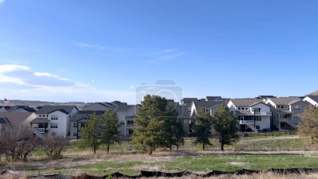 This image captures a serene suburban setting, showcasing a row of modern homes with distinct architectural styles, set against a backdrop of a clear blue sky and surrounded by natural greenery.