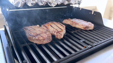 Photo for A person uses tongs to flip juicy steaks on a grill, with flames licking the meat, captured in a moment of intense heat and sizzle, showcasing a classic outdoor cooking experience. - Royalty Free Image