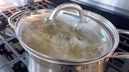 Téléchargez les photos : Capturée dans une cuisine maison, cette image dispose d'un pot en acier inoxydable avec de l'eau bouillante sur une cuisinière à gaz, mettant en valeur une étape de préparation culinaire commune avec de la vapeur montant du pot sous naturel - en image libre de droit