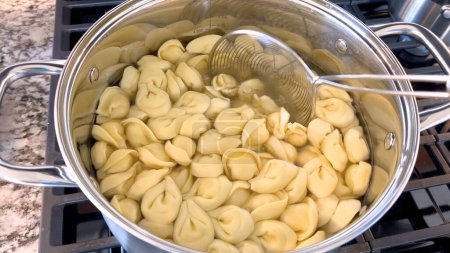 Téléchargez les photos : Une grande casserole remplie de pâtes tortellini bouillantes met en valeur la préparation de ce plat italien traditionnel, avec les pâtes flottant dans l'eau prête à être servie, posée sur un poêle à gaz moderne. - en image libre de droit