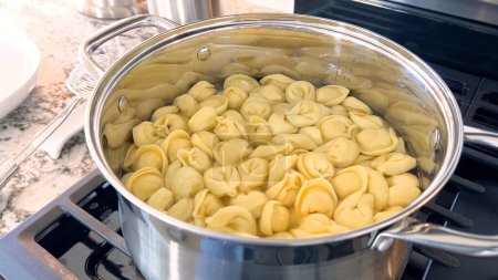 Foto de Una olla grande llena de pasta tortellini hirviendo muestra la preparación de este plato tradicional italiano, con la pasta flotando en agua lista para ser servida, colocada en una moderna estufa de gas. - Imagen libre de derechos