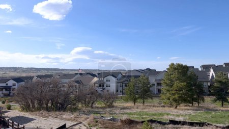 Esta imagen captura un entorno suburbano sereno, mostrando una fila de casas modernas con estilos arquitectónicos distintos, situadas sobre un telón de fondo de un cielo azul claro y rodeado de vegetación natural.