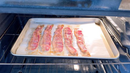 Crispy bacon strips bake evenly on a parchment-lined tray inside an oven, showcasing a clean and efficient method for achieving perfectly cooked bacon with minimal mess.