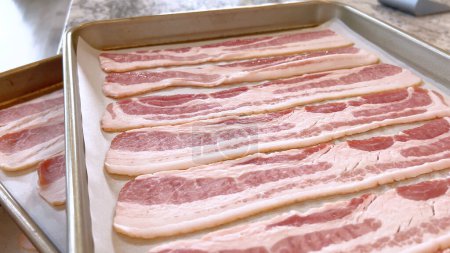 Neatly arranged raw bacon strips on a baking tray, prepared for cooking, capturing the fresh, uncooked look of this popular breakfast ingredient before it turns crispy and golden.