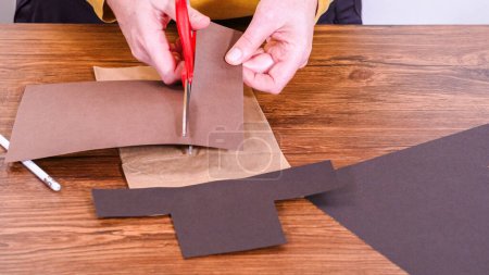 Schritt für Schritt. Der Lehrer führt den Online-Unterricht durch die Herstellung einer Papierpuppe aus einer braunen Tasche, wobei er eine Holzoberfläche kreativ als Arbeitsplatz nutzt.