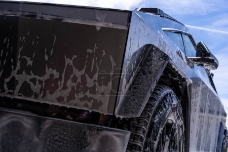 Photo for Denver, Colorado, USA-May 5, 2024-Close-up image of a Tesla Cybertruck being washed, showcasing the vehicle angular design and rugged tires. Water and soap suds cover the metallic surface - Royalty Free Image