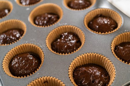 The process involves carefully scooping the rich batter into the waiting cupcake pan.