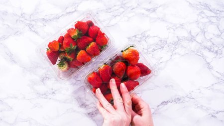 Flach lag er. Frische Erdbeeren werden in ihrem ursprünglichen, im Laden gekauften Plastikbehälter präsentiert, der auf einer Küchentheke liegt, bereit, gewaschen, gegessen oder gelagert zu werden..