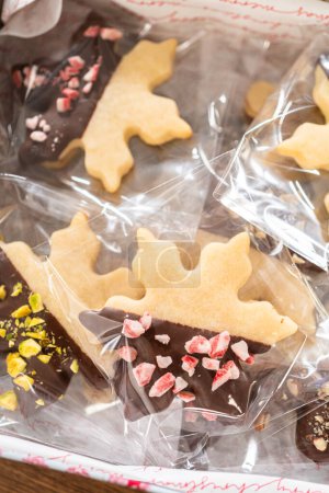 Lovingly homemade gingerbread and sugar cookies, half-dipped in rich chocolate, nestled in decorative Christmas tin boxes perfect for seasonal gifting.