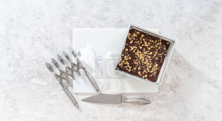 Flat lay. Removing chocolate hazelnut fudge from a square cheesecake pan lined with parchment.