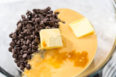 Schmelzen von Schokoladenstücken und anderen Zutaten in einer gläsernen Rührschüssel über kochendem Wasser zur Herstellung von Schokolade-Haselnuss-Fudge.