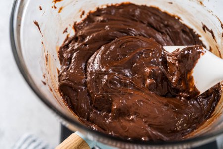 Melting chocolate chips and other ingredients in a glass mixing bowl over boiling water to prepare chocolate hazelnut fudge.
