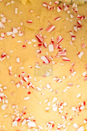 Filling square cheesecake pan lined with parchment paper with fudge mixture to prepare candy cane fudge.