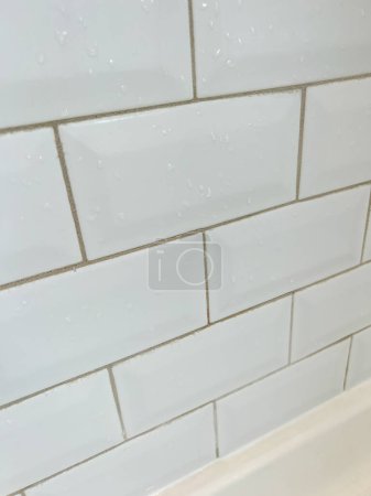 Close-up of a white tiled shower wall, showcasing the neat alignment of tiles and the presence of water droplets. This image highlights the clean and modern design of a shower area, emphasizing the