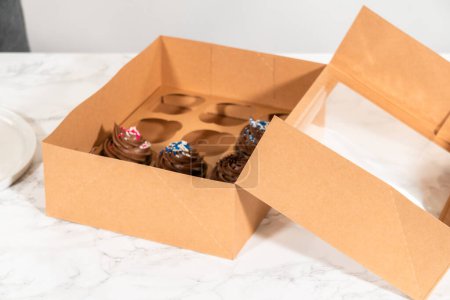 Preparing to share the delicious chocolate cupcakes, the final step involves carefully packaging them into a brown paper cupcake box.