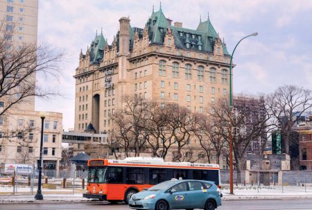 Téléchargez les photos : Winnipeg, Manitoba, Canada - 11 17 2014 : Un autobus orange de Winnipeg Transit et une cabine bleue Unicity Taxi circulant le long de la rue Main devant le bâtiment de l'hôtel Fort Garry érigé en 1913. Hôtel Fort Garry - en image libre de droit