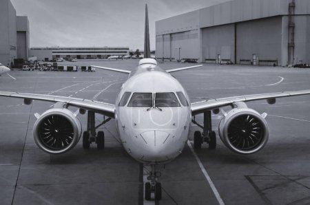Frontansicht eines modernen Twinjet-Flugzeugs, das auf dem Beton-Asphalt mit Spurmarkierungen in einem großen Flughafen sitzt. Schwarz-Weiß.