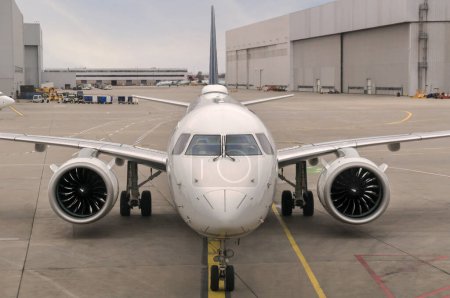 Frontansicht eines modernen Twinjet-Flugzeugs, das auf dem Beton-Asphalt mit Spurmarkierungen in einem großen Flughafen sitzt.