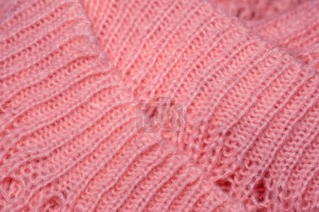 Vue détaillée d'un pull tricoté rose doux, présentant des points et une texture complexes.