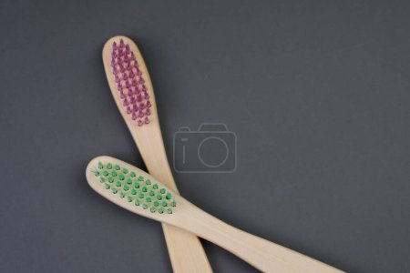 Two basic wooden toothbrushes, one with green bristles and the other with pink bristles, laid out on a flat surface.