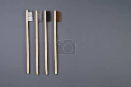 Three eco-friendly bamboo toothbrushes are arranged neatly on a solid gray background. The toothbrushes are unmarked and show the natural grain of the bamboo material.
