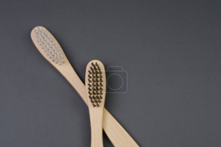 Two wooden toothbrushes are placed side by side on a flat surface. The brushes are made of wood with bristles at the top.