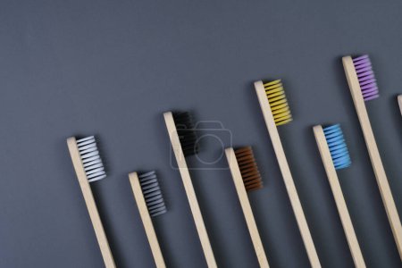 A straight row of toothbrushes neatly lined against a plain gray background, showcasing their handles and bristles in a clean and organized manner.