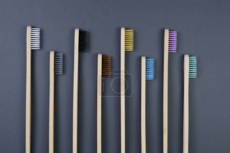 Téléchargez les photos : Une variété de brosses à dents en différentes couleurs soigneusement disposées dans une rangée sur un fond gris uni. - en image libre de droit